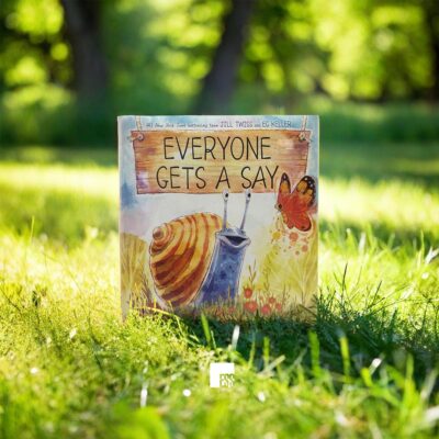 The book 'Everyone Gets A Say' by Jill Twiss and Eg Keller, set in a sunny meadow.