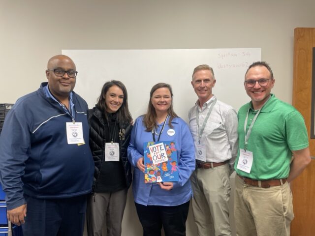 A group of Election Systems & Software employees hand giveaway winner and Marion County Clerk Kate Sweeney Bell her giveaway book.